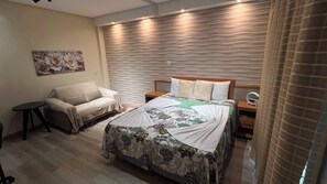 A hotel room with a bed, a sofa, a small table, and a wall-mounted light fixture. - 401 Suite Elegante e Moderna (Belém)