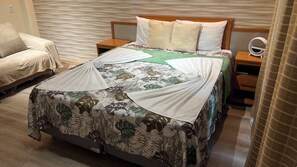 A neatly made bed with a floral bedspread, a bedside table with a mirror, and a chair in a hotel room. - 401 Suite Elegante e Moderna (Belém)