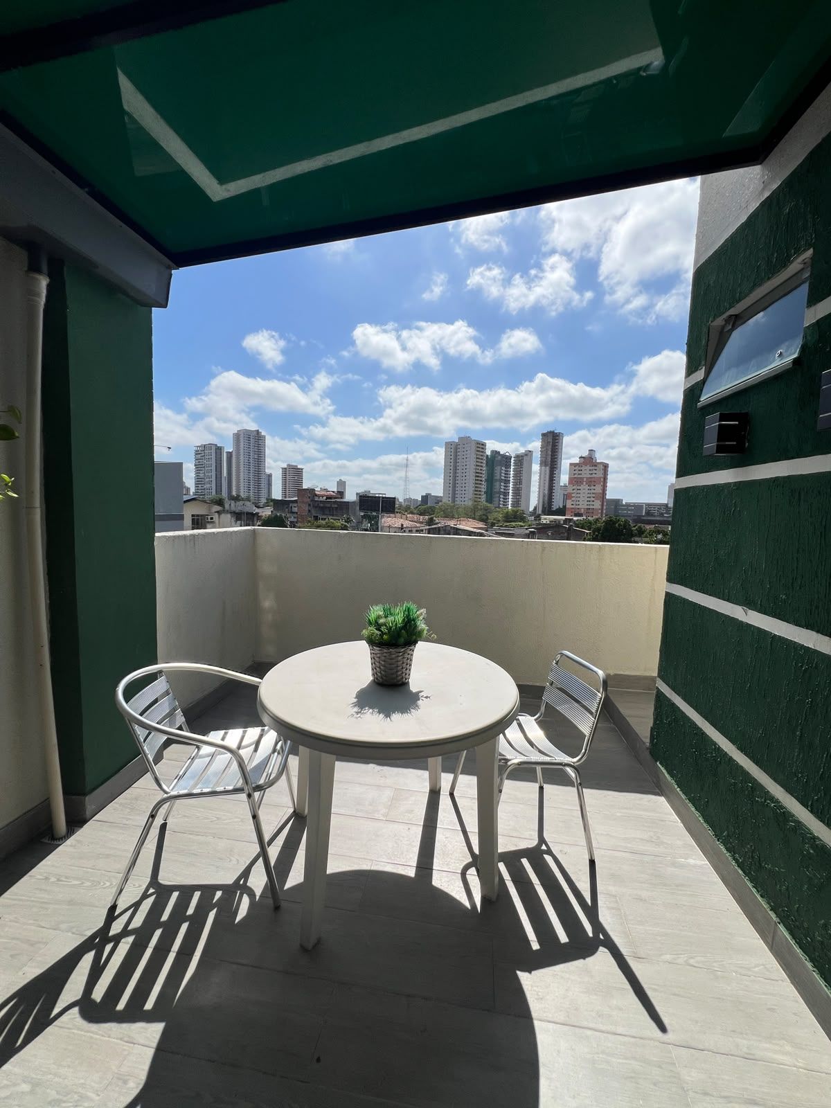 Un balcon avec une table ronde et deux chaises, un pot de fleurs et une vue sur le paysage urbain.