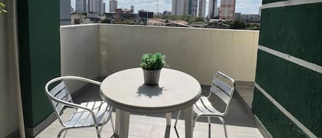 Un balcon avec une table ronde et deux chaises, un pot de fleurs et une vue sur le paysage urbain.