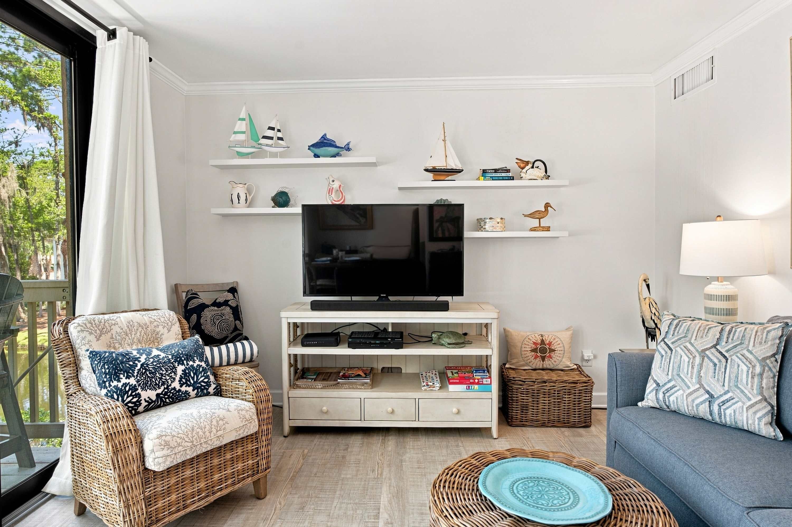 Uma sala de estar com televisão, móveis de vime e objetos decorativos nas prateleiras.