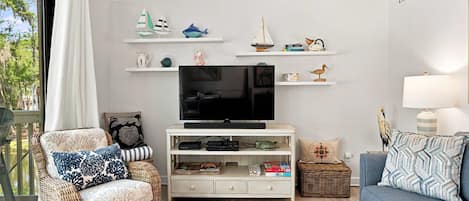 Una sala de estar con televisor, muebles de mimbre y objetos decorativos en estanterías.