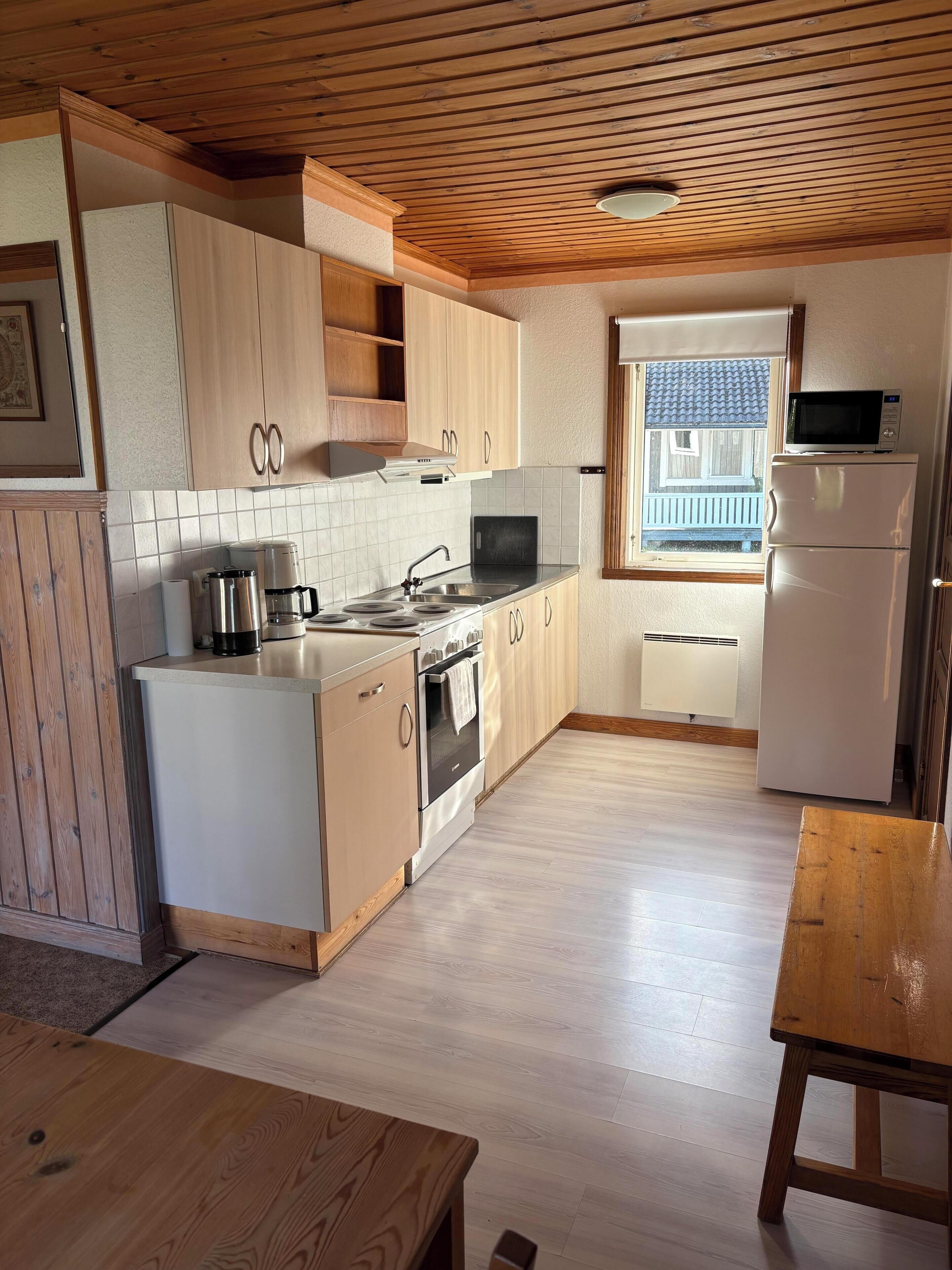A kitchen with wooden cabinets, a stove, a microwave, and a refrigerator.