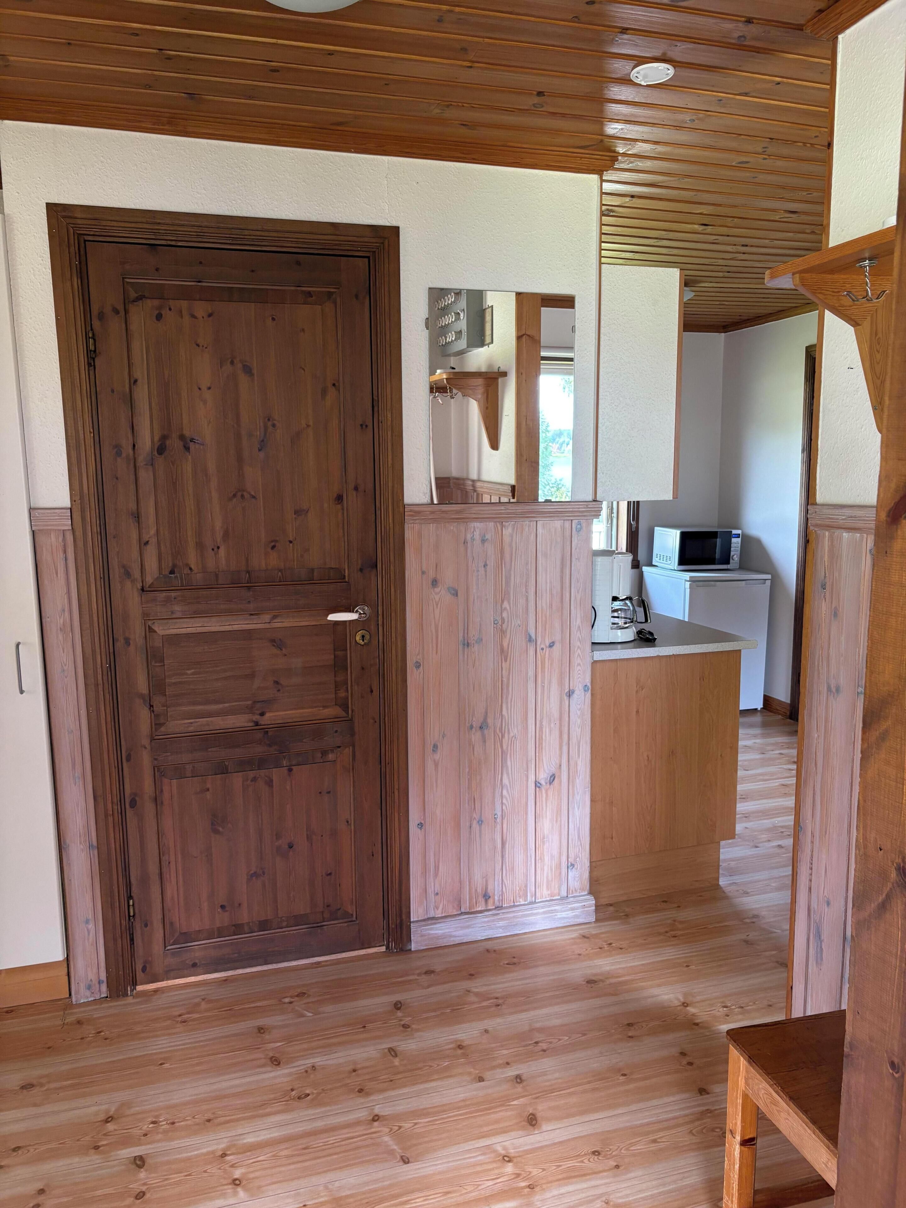 Een houten deur, een keuken met een magnetron, en een houten vloer.