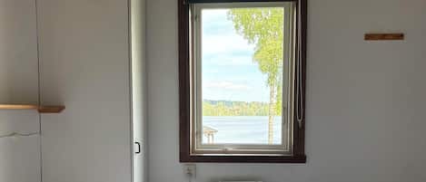 A bedroom with a bed, a window with a view of a lake, and a wooden ceiling.