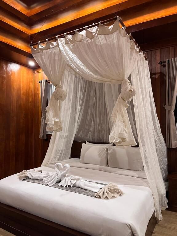A four-poster canopy bed with a white bedspread and pillows, a neatly folded towel on the bed, and wooden paneling on the walls.