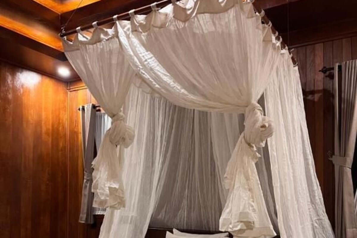Ein Bett mit Himmelbett, ausgestattet mit einer weißen Bettdecke und Kissen, ein ordentlich gefaltetes Handtuch auf dem Bett und Holzvertäfelung an den Wänden.