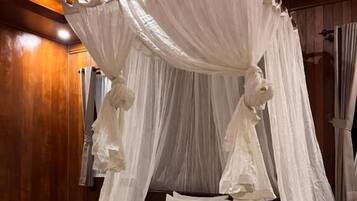 A four-poster canopy bed with a white bedspread and pillows, a neatly folded towel on the bed, and wooden paneling on the walls.