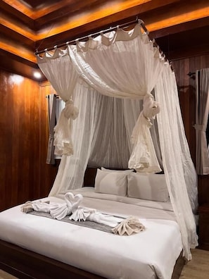 Ein Bett mit Himmelbett, ausgestattet mit einer weißen Bettdecke und Kissen, ein ordentlich gefaltetes Handtuch auf dem Bett und Holzvertäfelung an den Wänden.