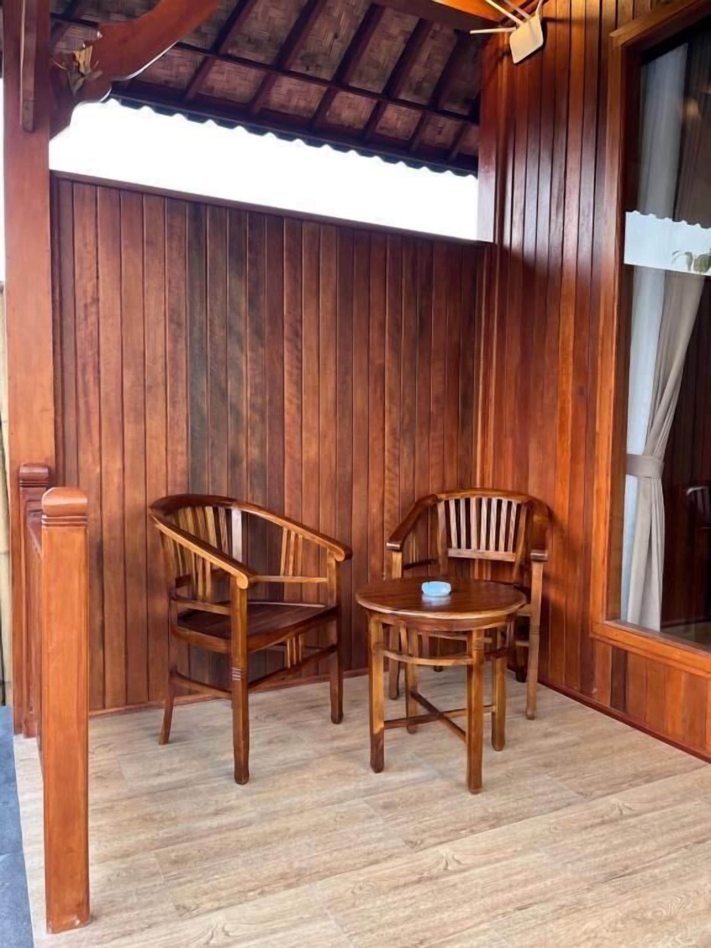 Una habitación de madera con dos sillas y una mesa, una ventana con cortinas y un techo de madera.