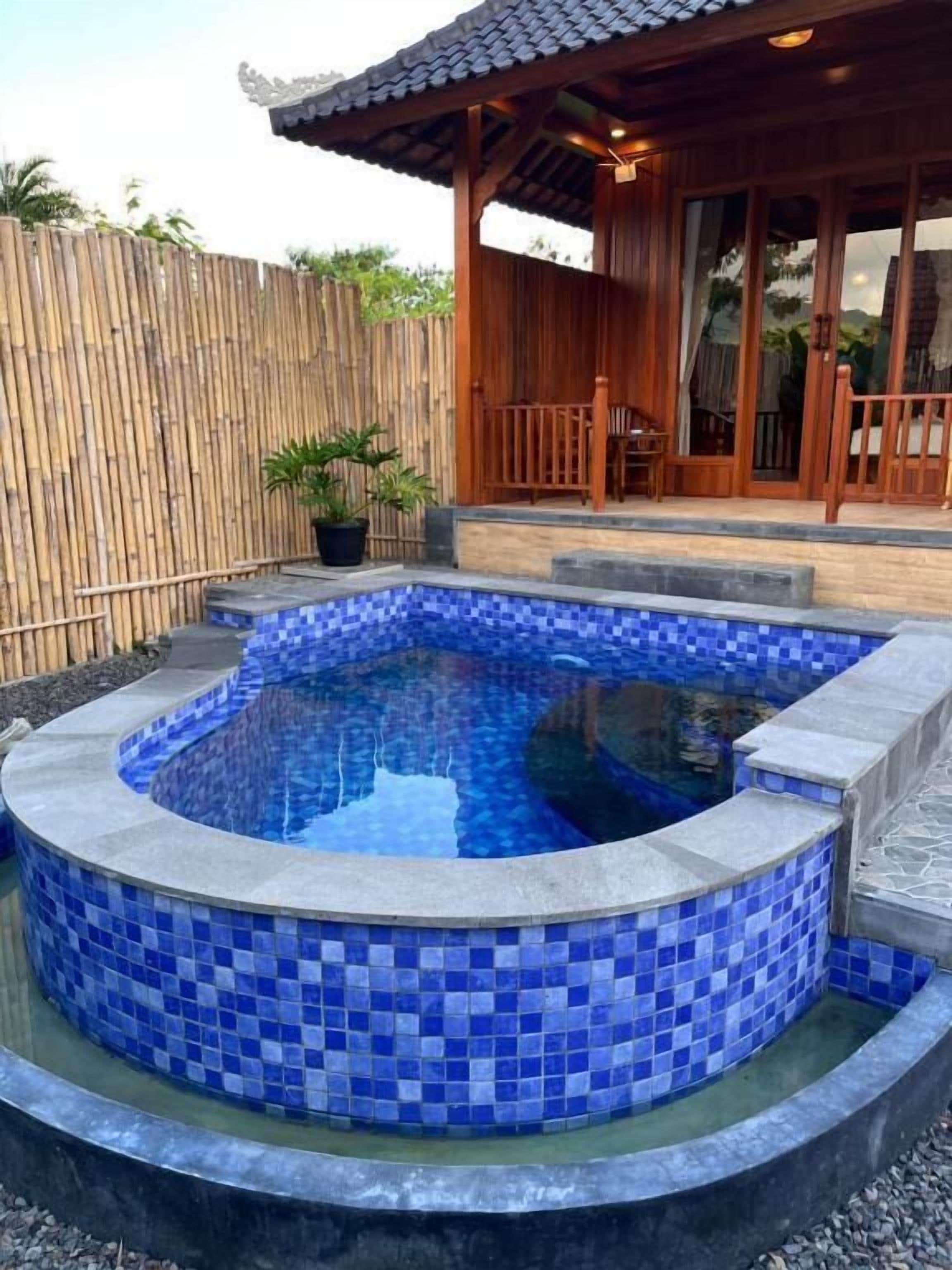 A hot tub with blue mosaic tiles, surrounded by a wooden deck and a bamboo fence.