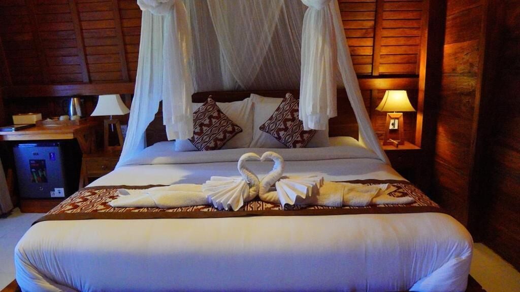 A hotel room with a bed, canopy, pillows, and a bedside table with a lamp.