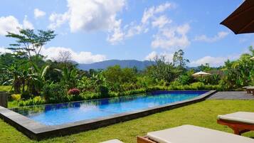 A swimming pool with a surrounding garden, lounge chairs, and a view of mountains.