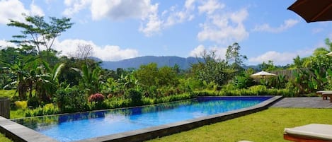 Piscina com jardim ao redor, espreguiçadeiras e vista para montanhas.