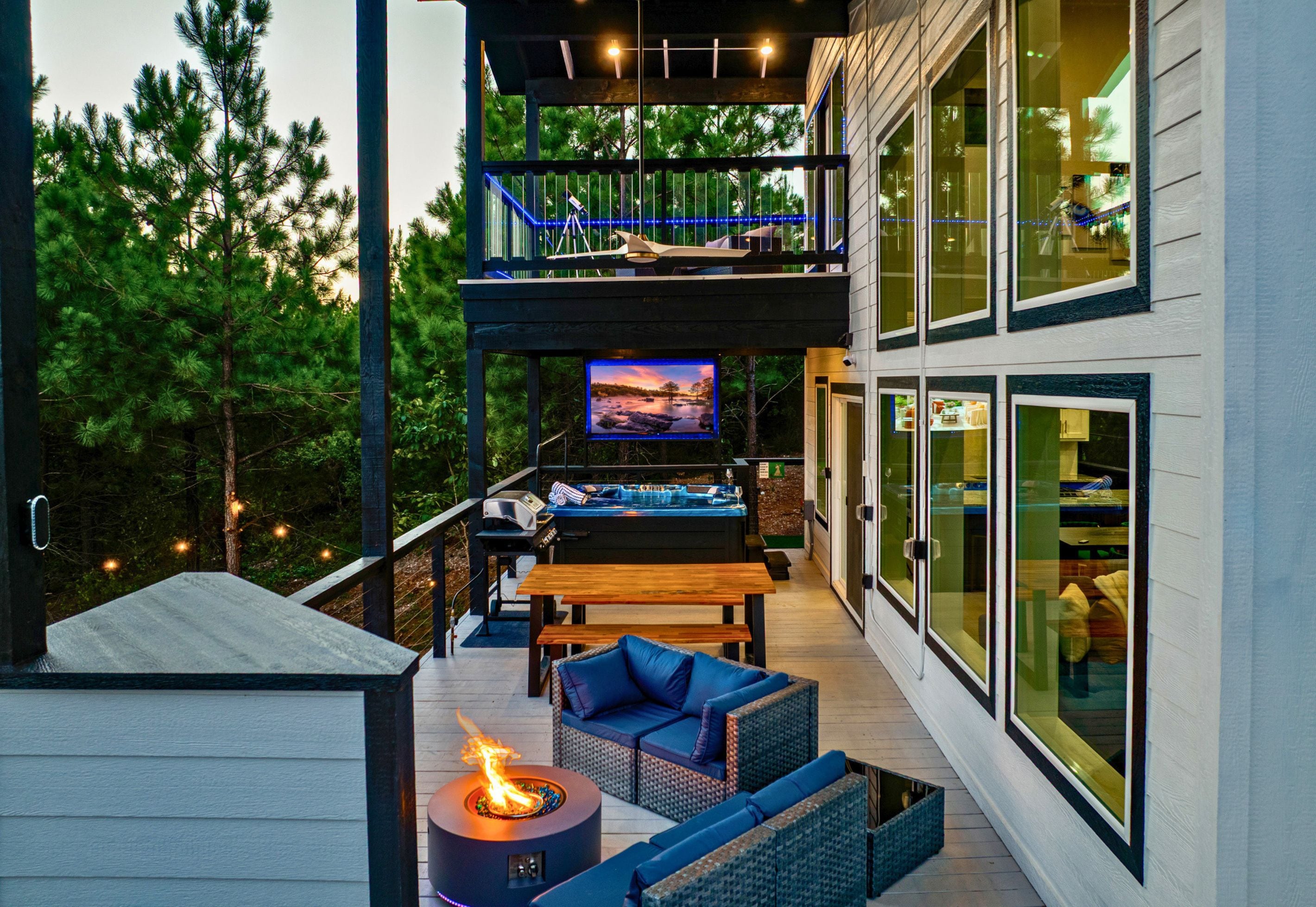 A modern outdoor deck with a fire feature, seating, and a TV screen.