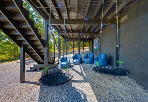 An outdoor seating area with swing seats and bean bags, a staircase, and a wall with a window. - Mountain Views | EV Charger | Pool | Speakeasy (Broken Bow)