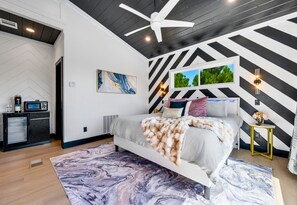 A modern bedroom with a bed, a ceiling fan, a black and white striped wall, and a window with a view of trees. - Mountain Views | EV Charger | Pool | Speakeasy (Broken Bow)