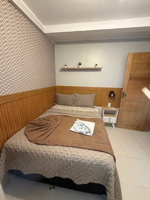 A bedroom with a bed, a nightstand, a wooden headboard, a herringbone-patterned wall, and a door. - 402 Funcional e Acolhedor (Belém)