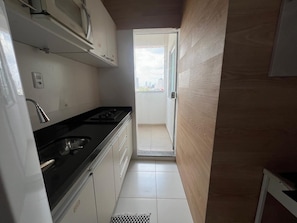 A narrow kitchen with a black countertop, white cabinets, and a view through an open door to a balcony. - 402 Funcional e Acolhedor (Belém)