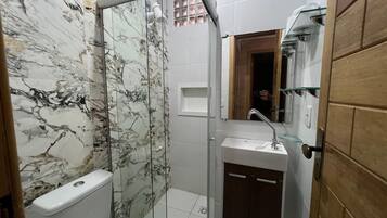 Un baño con cabina de ducha de vidrio, inodoro, lavabo con espejo y puerta de madera.