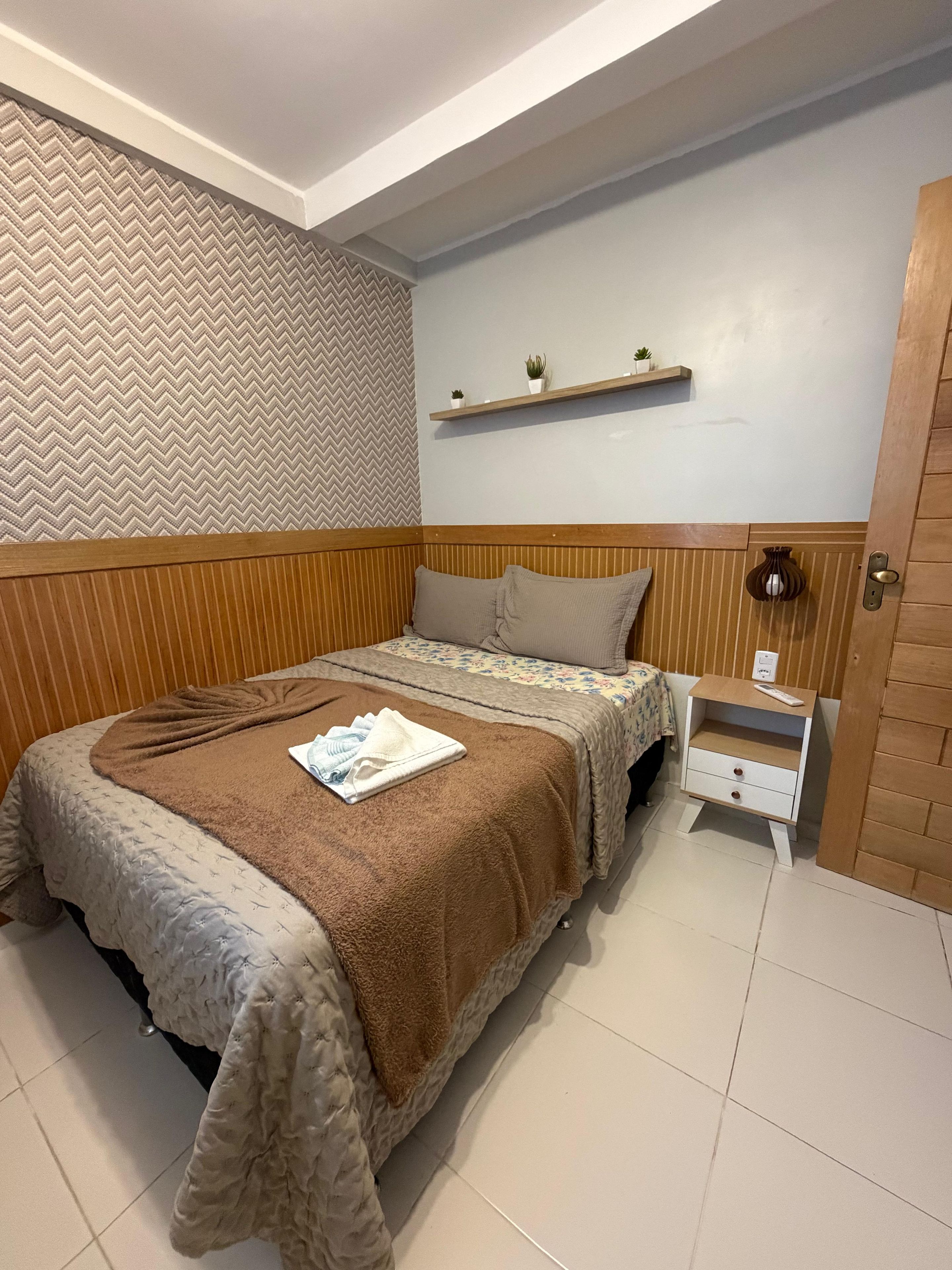 Una cama bien hecha con una manta marrón, una mesita de noche con una lámpara y un cabecero de madera.