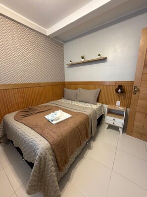 A neatly made bed with a brown blanket, a bedside table with a lamp, and a wooden headboard. - 402 Funcional e Acolhedor (Belém)