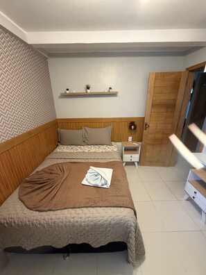 Un dormitorio con cama, mesitas de noche, cabecera de madera, pared con diseño de espiga y una puerta.