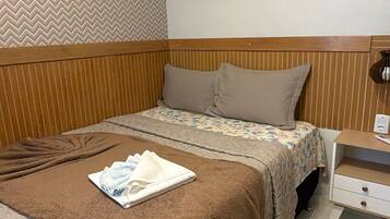 Un dormitorio ordenado con una cama, almohadas, una mesita de noche y una estantería con plantas.