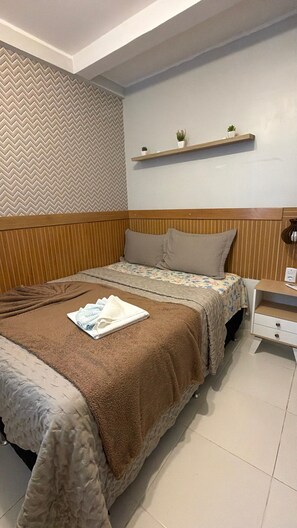 A neatly arranged bedroom with a bed, pillows, a bedside table, and a wall-mounted shelf with plants. - 402 Funcional e Acolhedor (Belém)