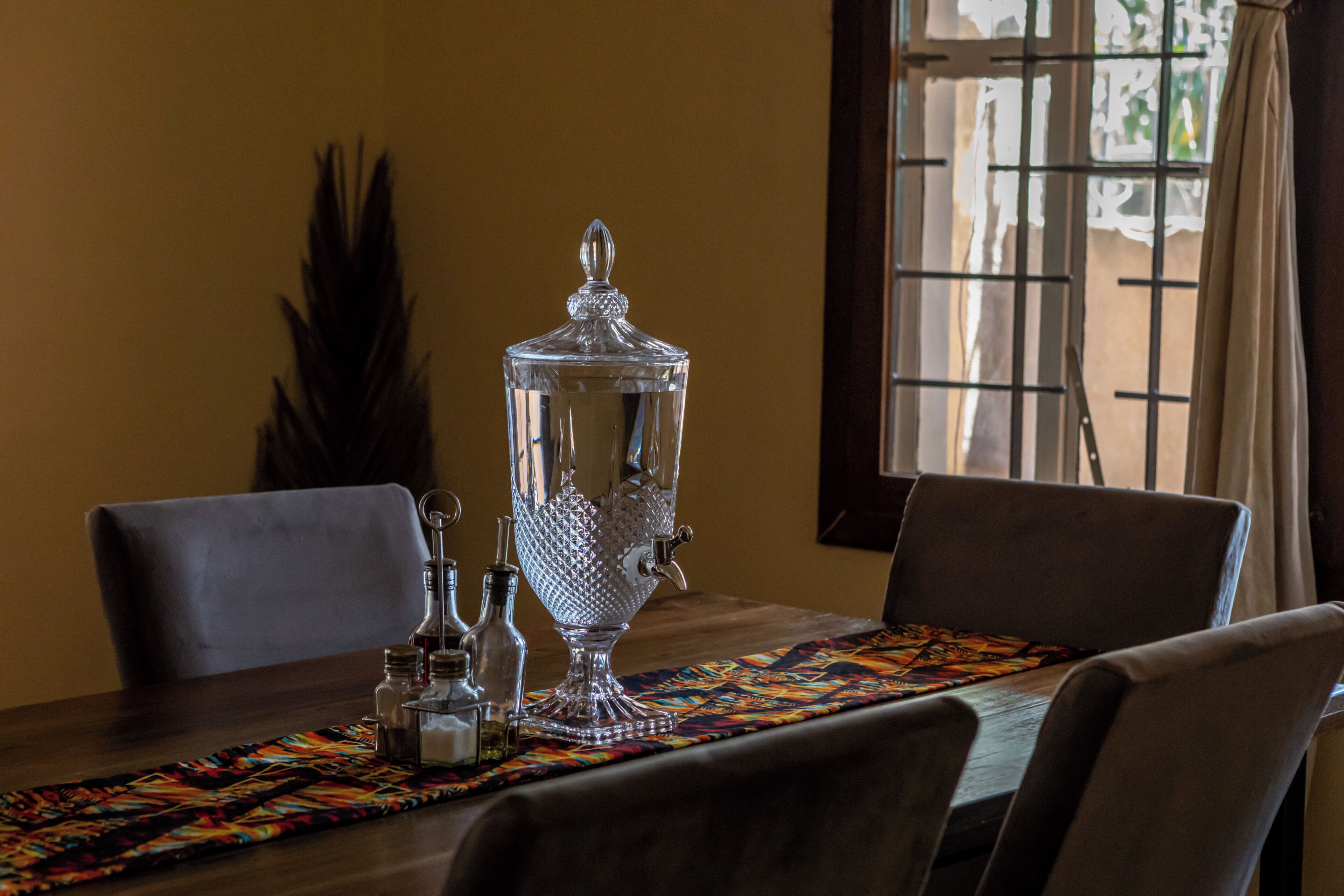A dining table with a decorative glass container, salt and pepper shakers, and a colorful placemat.