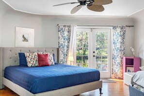 Un dormitorio con cama, ventilador de techo, ventana con cortinas y vistas al exterior.