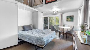 Een moderne slaapkamer met een bed, een eethoek met tafel en stoelen, en een glazen schuifdeur naar een balkon.