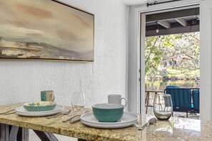A dining area with a granite countertop, a painting above, and a view of a garden through an open door. - Double Waterfront Estate; 12 Beds, Kayaks, Firepit (Tampa)
