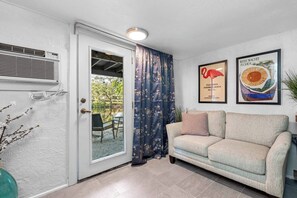 A living room with a sofa, a door leading to an outdoor area, and two framed pictures on the wall.