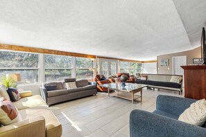 A spacious living room with a large window, a sofa, a coffee table, and a blue armchair. - Double Waterfront Estate; 12 Beds, Kayaks, Firepit (Tampa)