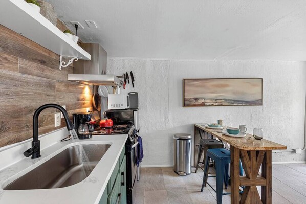 A modern kitchen with a built-in stove, sink, and a wooden dining table with bar stools.
