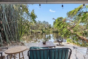 An outdoor seating area with a view of a calm lake, surrounded by bamboo and trees. - Double Waterfront Estate; 12 Beds, Kayaks, Firepit (Tampa)