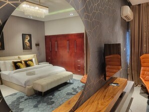A hotel room with a bed, a wooden side table, a mirror, a wardrobe, and a seating area with a chair. - 4 units of 2bedroom building in gorgeous Lagos with AC and fitness room (Lagos)