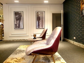 Ein modernes Interieur mit zwei Sesseln, einem kleinen Tisch und gerahmten Kunstwerken an der Wand.