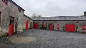 A gravel courtyard with multiple red doors and windows on a stone building.