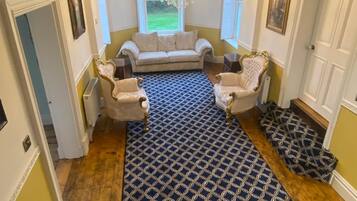 A living room with a patterned rug, a sofa, two armchairs, a chandelier, and a window with a view.