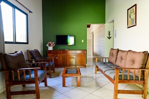 A living room with a green wall, a television, wooden furniture, and a tiled floor. - Casa do Curral | A home close to everything! (Ilhabela)