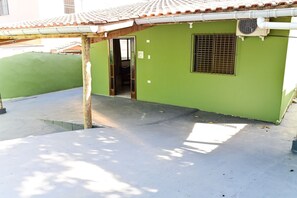 A green building with a tiled roof, a small window with bars, and a door leading to an interior space. - Casa do Curral | A home close to everything! (Ilhabela)