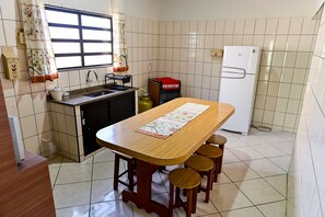 A compact kitchen with a wooden table, stools, a sink, and a refrigerator. - Casa do Curral | A home close to everything! (Ilhabela)