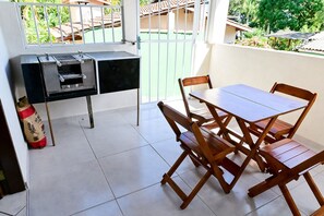 A balcony with a grill, a table, and chairs. - Casa do Curral | A home close to everything! (Ilhabela)