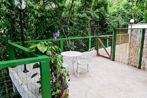 Ein Terrassenbereich mit Tisch und Stühlen, umgeben von einem grünen Zaun und üppiger Bepflanzung.