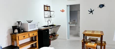 A bedroom with a bed, a wooden dresser, a kitchenette with a microwave, and a small table with chairs.
