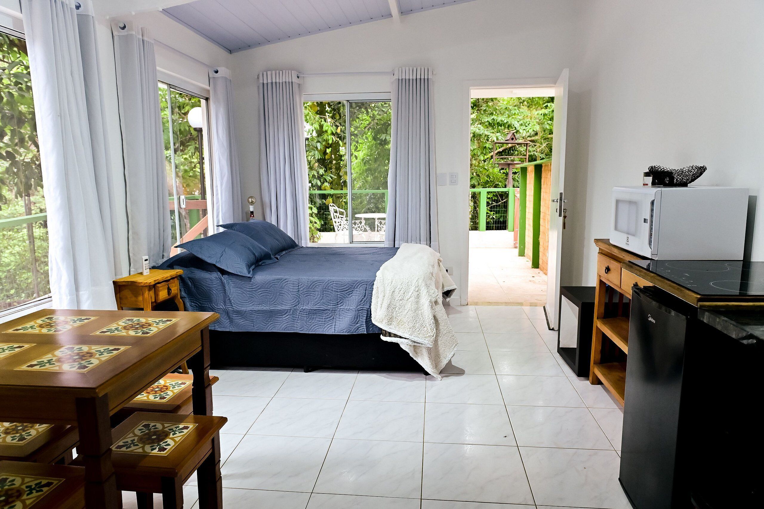 A bedroom with a bed, a bedside table, a chair, a window with curtains, and a view of greenery outside.