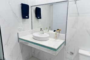 Ein Badezimmer mit weißem Waschbecken, einem Spiegel und einem Handtuchhalter.