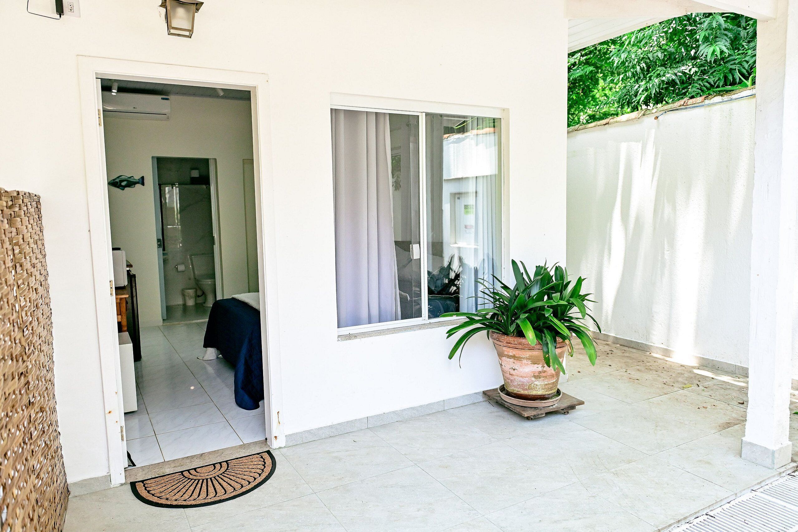 A clean, well-lit entrance with a door leading to a room, a window with curtains, and a potted plant on the floor.